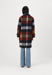 Manteau en laine présentant un motif tartan multicolore avec des tons marine, orange et crème. Col cranté, manches longues et poignets à boutons.
