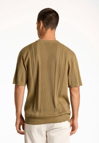 Kortärmad, olivgrön stickad tröja med vertikal ribbad struktur och avslappnad passform, med rundad halsringning och subtila fålldetaljer.