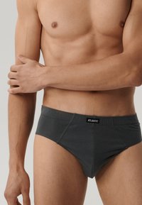 Ciemnoszare slipki wykonane z miękkiego materiału, z elastycznym paskiem z logo i dopasowanym krojem. Projekt zawiera gładką fakturę i bezszwowe boki.