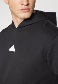 Felpa nera con cappuccio realizzata in tessuto morbido, con un logo bianco sul petto. Il design include un cappuccio e una vestibilità comoda.