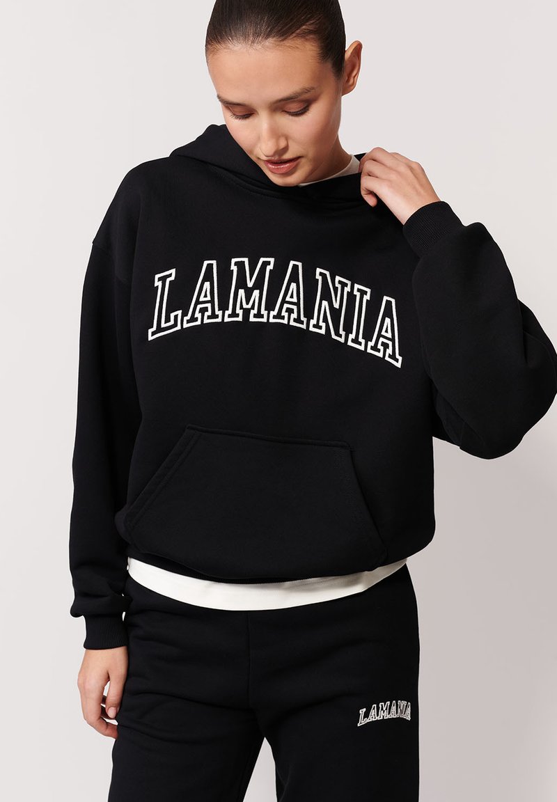 Czarna bluza z kapturem z białym napisem "LAMANIA", kieszenią z przodu i ściągaczami. W połączeniu z czarnymi spodniami dresowymi z haftowanym logo. G�ładki materiał.