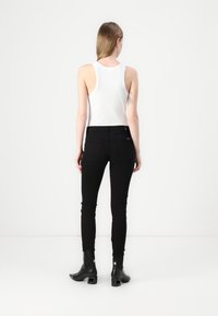 Top sin mangas blanco combinado con jeans ajustados negros y botas negras brillantes hasta el tobillo con tacón cuadrado. Diseño simple y ajustado.