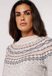 Helles graues Strickpullover mit einem Muster aus dunkelgrauen und pfirsichfarbenen Streifen sowie geometrischen Designs um den Schulternacken und einem hohen Kragen.