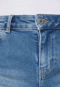 Modré denimové džíny s klasickým pasem, kovovým zapínáním na knoflík a jemným prošíváním. Tkanina má hladkou texturu s mírným vyblednutím.