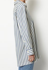 Striped shirt in cream and navy blue, featuring a collar, long sleeves with button cuffs, and a loose fit. Made from a lightweight fabric.