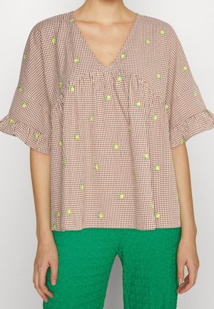 Bluzka z krótkim rękawem i dekoltem w serek w brązową kratę i drobny żółty kwiatowy wzór, zestawiona z teksturowanymi, jasnorozzielonymi spodniami.