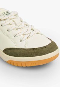 Weißes Leder-Sneaker mit olivgrünen Wildlederdetails, orangefarbenen Nähten und einer Gummisohle. Die Schnürsenkel sind klassisch weiß mit sichtbaren Nähten.