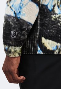Gros plan sur le bras d'une personne portant un pull en tricot multicolore avec un petit logo Nike brodé sur le poignet.