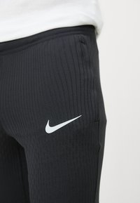 Melnas sporta leggins ar ribotu tekstūru un baltu Nike logo kreisajā augšstilbā. Elastīga josta nodrošina labu piegulšanu un komfortu.