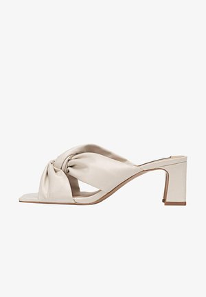 Mule beige à bout ouvert avec des brides rembourrées torsadées et un talon bloc de hauteur moyenne sur fond blanc.