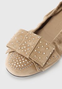 Μπεζ σουέντ επίπεδο παπούτσι με στρογγυλεμένη μύτη, διακοσμημένο με μεγάλο φιόγκο και τρουκς. Μαλακή υφή με λαμπερές στρας λεπτομέρειες.