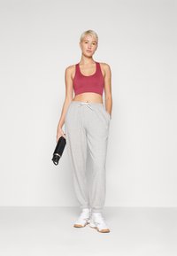 Calças de treino cinzentas com punhos elásticos, combinadas com um top curto bordeaux e ténis brancos. A pessoa segura uma garrafa de água preta.