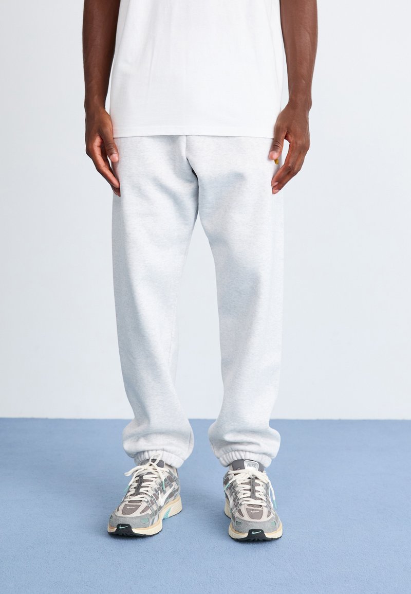 Light grey sweatpants with cuffed ankles, made from soft fabric, paired with patterned running shoes in shades of grey and teal.