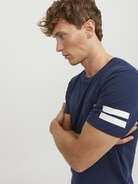 Marineblå bomulds t-shirt med korte ærmer, der har to hvide striber på venstre ærme. Glat tekstur og normal pasform.