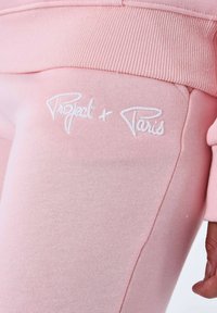 Pantalones de chándal rosa con el logotipo bordado "Project + Paris" en blanco. Hechos de un tejido suave, con una cinturilla acanalada y una textura lisa.