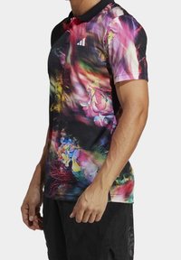 Camicia a maniche corte multicolore con motivo floreale, realizzata in tessuto leggero con colletto nero a tinta unita e logo Adidas.