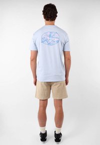 Camiseta de algodón azul claro con un estampado gráfico colorido en la parte posterior, combinada con pantalones cortos beige y zapatillas negras.