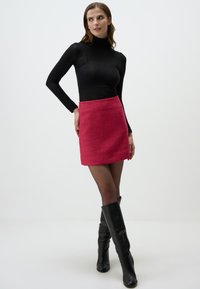 Fitted black turtleneck, textured pink mini skirt, and knee-high black boots. Skirt features a subtle pattern, creating visual interest.