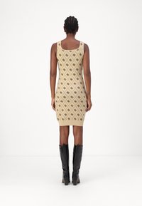 Robe en tricot beige avec motif géométrique noir, design ajusté, décolleté boat, longueur mi-cuisse, associée à des bottes noires jusqu'aux genoux.