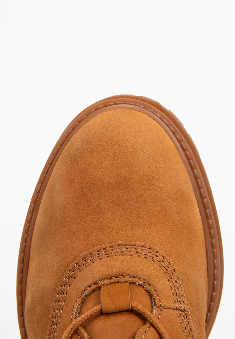 Botín de ante marrón hasta el tobillo con puntera redonda, que presenta costuras en tono y suela de goma. Cierre de cordones en la parte delantera.