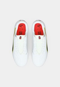 Białe buty sportowe z teksturowaną, syntetyczną cholewką, czarnymi i neonowożółtymi akcentami oraz czerwonymi wkładkami. Posiadają sznurowadła i wentylowaną konstrukcję.