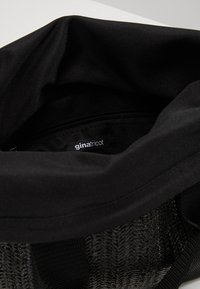 Bolsa negra con una base de malla texturizada negra, un forro de tela suave y un cierre de cremallera. La etiqueta interior dice "ginatricot."