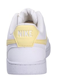 Sneaker bianca in pelle con superficie testurizzata, dotata di un accento giallo sul tallone e un logo bianco. Forma arrotondata e collare imbottito.