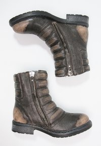 Hnědé ankle boots s texturovaným koženým svrškem, vroubkovaným designem a bočními zipy. Černá gumová podrážka pro odolnost.