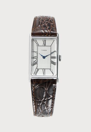 Montre Timex rectangulaire argentée avec cadran blanc, aiguilles bleues des heures et des minutes, chiffres romains noirs et bracelet en cuir brun foncé texturé.