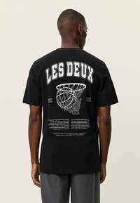 Μαύρο βαμβακερό t-shirt με μεγάλο λευκό κείμενο στην πλάτη, γραφικό με μπασκετικό καλάθι και εκτυπωμένο κείμενο με περιγραφικές λεπτομέρειες.