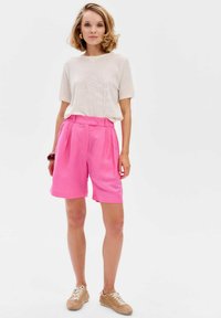 Lichte, geperforeerde t-shirt met een crème kleur en felroze high-waisted shorts, gecombineerd met beige veterschoenen.