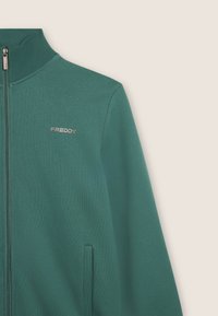 Giacca zip-up verde scuro realizzata in un morbido tessuto testurizzato. Caratterizzata da un colletto alto, tasche laterali e un logo argento "FREDDY" sul petto.