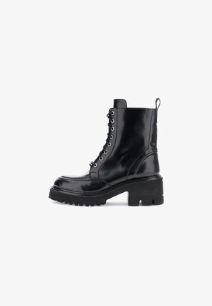 Bottine noire en cuir à lacets avec une semelle épaisse, bout arrondi, finition soignée et œillets en métal. Elle présente une languette sur le talon.