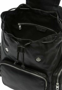 Czarny skórzany plecak z zapięciem na sznurek, srebrnymi elementami oraz przednią kieszenią na zamek z teksturowanym wykończeniem. Wnętrze wyłożone podszewką i przestronne.