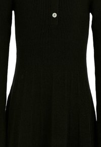 Primo piano di un vestito nero a maglia a costine con maniche lunghe e un dettaglio di bottoni frontali vicino al colletto.