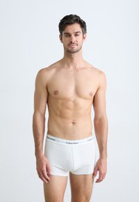Calvin Klein hvide bomulds boxer briefs med en elastisk talje, der har et logo, vist på en mandlig model mod en lys baggrund.