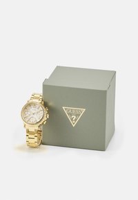 Gold watch with a linked band, round face, and chronograph features. Accompanied by a textured green box with gold branding.