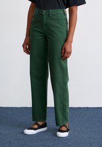 Green high-waisted wide-leg jeans made of cotton, featuring a button closure, front pockets, and a smooth texture. Worn with black shoes.