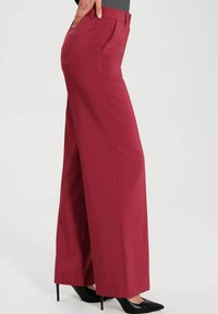 Breda byxor i en rik bordeauxfärg, med en slät finish, skräddarsydd passform och sidofickor. Bärs med svarta högklackade skor.