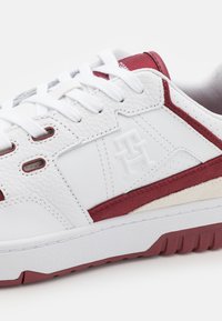 Baskets blanches avec accents bordeaux, tige en cuir texturé, col rembourré, détails perforés et semelle en caoutchouc.