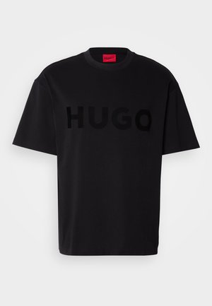 T-shirt in cotone nero con maniche corte, colletto tondo, caratterizzata da un grande logo lucido nero "HUGO" sul davanti. Texture liscia.