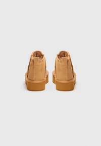 Botas de tobillo de ante en color tostado, con forro suave, punta redondeada y suela plana de goma, que cuentan con una lengüeta en la parte trasera para facilitar su uso.