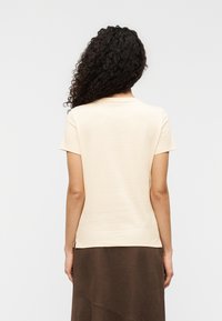 Μπεζ κοντομάνικο μπλουζάκι με απλό λαιμόκοψη. Μαλακή υφή, εφαρμοστή σχεδίαση και πλαϊνές σχισμές κοντά στο τελείωμα. Φορεμένο με καφέ φούστα.