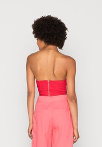 Top vermelho sem alças com fecho zíper nas costas, combinado com calças rosa de cintura alta. Textura suave e ajuste bem definido visíveis.