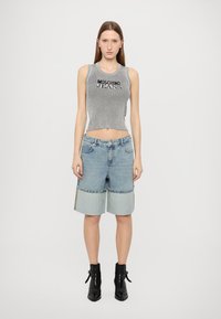 Grå ribbet crop-top med teksten "MOSCHINO JEANS"; blå denimshorts, vidde, lys blå kant; kombinert med svarte ankelstøvler.