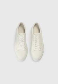 Λευκά δερμάτινα αθλητικά παπούτσια με επίπεδα κορδόνια, στρογγυλεμένη μύτη και διακοσμητικά καρφιά κατά μήκος της σόλας. Ομαλή υφή με ελάχιστες λεπτομέρειες και διακριτικό λογότυπο.