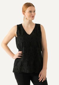Top negro sin mangas con escote en V, patrón de encaje intrincado y dobladillo con formas onduladas. Combinado con pantalones negros ajustados para un look cohesivo.