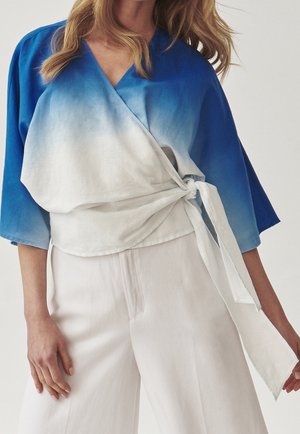 Een blauw-witte gradient wrap top met driekwart mouwen, gestrikt in de taille, gecombineerd met witte wijde broekspijpen. Glad stoftextuur.