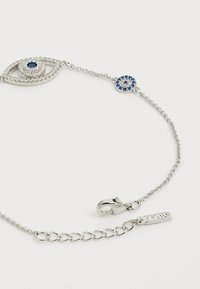 Pulsera de cadena de plata con un diseño en forma de ojo, con una piedra azul en el centro, rodeada de piedras transparentes, y un acento de piedra azul redonda.