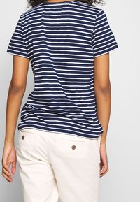 Granatowo-biała koszulka w paski z krótkimi rękawami i okrągłym dekoltem, wykonana z bawełny, noszona z jasnymi spodniami.